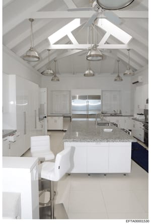This is a photograph of a contemporary kitchen space featuring white cabinetry, granite countertops, stainless steel appliances, and an open floor plan with vaulted ceilings and skylights. The image appears to be documentation of interior design or p