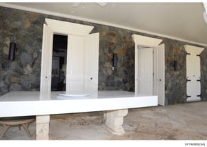 This photograph shows an interior room or hallway of a high-end residential property during renovation or construction phase. The space features distinctive slate or stone accent walls in gray and brown tones, white trim and doorframes, a white curve