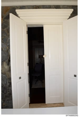 This is an evidence photograph showing an interior room with white double doors opening into a darkened space containing office furniture, including a black office chair. The photo documents the architectural features and interior layout of what appe