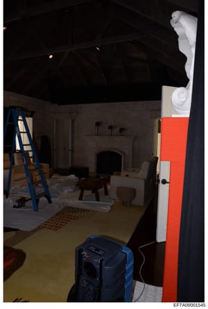 This photograph shows an interior room in mid-renovation or construction, featuring a fireplace, ornate white architectural details, and various construction equipment. The image appears to be evidence documentation from a property inspection related