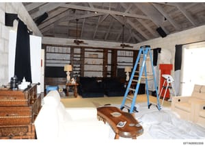 This is an evidence photograph showing the interior of a large room or open living space in what appears to be a residential property. The space is undergoing renovation or construction, with exposed wooden beam ceiling, work ladders, covered furnitu