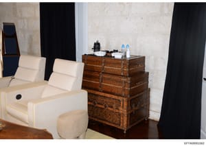 This is a photograph of an interior space showing luxury furnishings and décor, including cream-colored seating furniture with gold trim, a decorative antique wooden trunk with metal hardware, and black curtains. The room features marble or stone wal