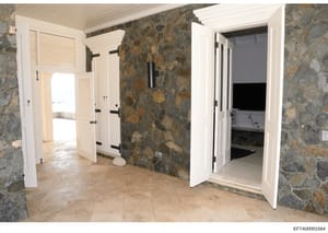 This is a photograph of an interior space featuring distinctive stone wall construction with tan and gray tones. The room contains multiple white-framed doorways and closets with louvered doors, suggesting this may be a residential hallway, bedroom, 