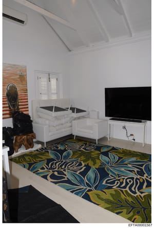 This photograph shows an interior living space featuring modern white sectional seating, a flat-screen television, decorative artwork, and a patterned area rug in blue, green, and cream tones. The room appears to be part of a residential property, wi