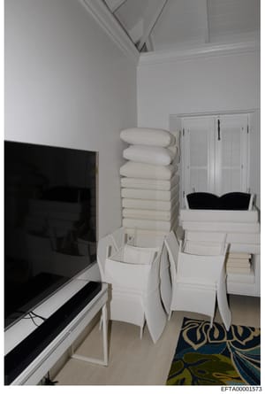 This is a photograph of an interior room space showing organized storage of white linens, towels, and bedding materials stacked on shelving and in white storage containers. A flat-screen television is visible on the left side of the frame. The image 