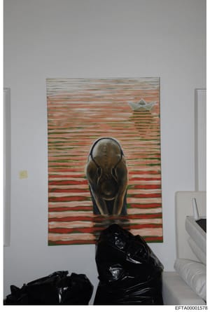 This is an evidence photograph showing the interior of a room with artwork hung on a white wall. The painting features a stylized bear figure in the foreground against a horizontally-striped background in red, green, and tan tones, with a paper boat 