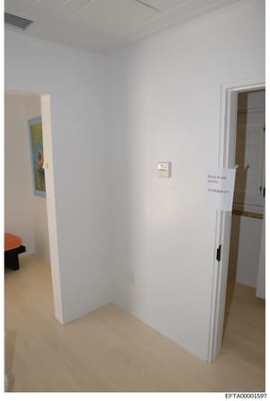 This is an evidence photograph showing an interior room with white walls, light wooden flooring, and what appears to be a bathroom entrance. A handwritten notice on the wall reads 'Please do not Use this BATHROOM!!!!' in blue ink, suggesting restrict