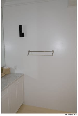 This is a photograph of a bathroom or utility room interior, showing white walls, a marble countertop, white cabinetry, a towel basket, electrical outlet, a towel rack, and a wall-mounted light fixture. The image appears to be documentary evidence ph