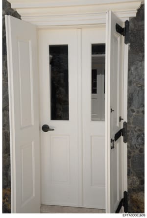 This is an evidence photograph showing the interior of a room or hallway featuring two white doors with glass panels and black hardware, set against textured gray stone or concrete walls. The photograph appears to be documentation of physical spaces,