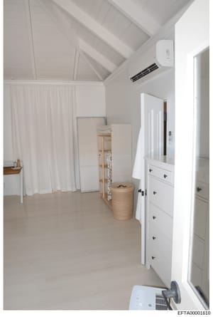 This is an evidence photograph showing the interior of a room with white walls, vaulted ceiling, and minimal furnishings. The space appears to be part of a residential property and contains white cabinetry, curtains, and storage items. This type of p