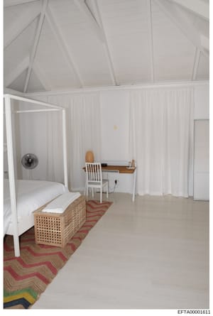 This is a photograph of a bedroom interior featuring a white canopy bed with wooden frame, a wooden desk with white chair, exposed beam ceiling, white curtain partitions, and a geometric patterned rug. The room appears to be part of a property docume