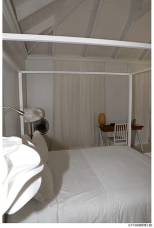 This is a photograph of a bedroom interior featuring a white four-poster canopy bed with sheer curtains, wooden furniture, and clean minimalist décor. The image appears to be evidence documentation from a property investigation, showing the bedroom's