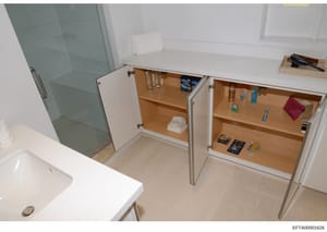 This photograph shows the interior of a bathroom with open medicine cabinet doors revealing stored items including toiletries, personal care products, and household supplies. The image documents the contents and layout of bathroom storage at what app