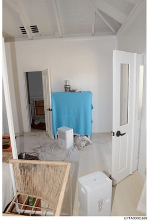 This photograph shows an interior room in the early stages of renovation or preparation, featuring white walls, ventilation systems in the ceiling, and various equipment and materials typical of construction or staging work. The room contains a blue-