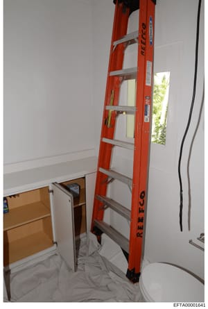 This is an evidence photograph showing an interior bathroom space with a red fiberglass ladder positioned against the wall, an open wooden cabinet, and a toilet visible in the foreground. The photo appears to be from a property search or inspection, 