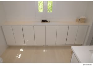 This is a photograph of a minimalist interior space showing a room with white built-in wall cabinetry, light wood flooring, and windows with natural light. The room contains minimal furnishings and appears to be part of a property documentation or ev