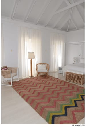 This is a photograph of an interior bedroom space, likely from one of the properties associated with the investigation. The room features contemporary minimalist design with white walls, exposed beam ceiling, natural light from sheer curtains, and mo