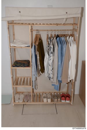 This is a photograph of a wooden wardrobe closet system containing an organized collection of clothing items and footwear. The image shows a portable clothing rack with multiple shelves, hanging rods for garments, and a bottom shelf displaying shoes.