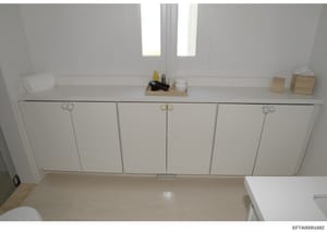 This is an overhead photograph of a bathroom interior showing a white vanity with six cabinet doors, countertop surfaces, and bathroom accessories. The image documents the physical space and layout of what appears to be a property under investigation