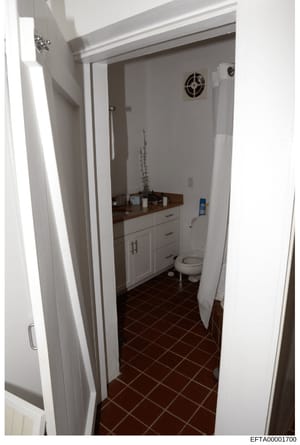 This is a photograph of a bathroom interior showing a white vanity cabinet with dark countertop, toilet, and dark tile flooring. The image appears to be evidence documentation from an investigation property inspection, likely taken to document the co