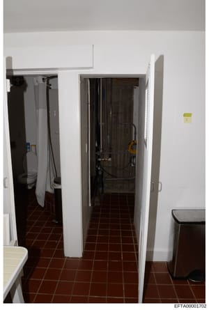 This is an evidence photograph showing an interior room with white walls, dark reddish-brown tile flooring, and multiple doorways. The space contains what appears to be utility closets or bathroom access points, with various equipment and materials v