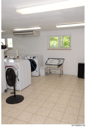 This is a photograph of a modern, well-equipped laundry facility featuring multiple washing machines, dryers, and auxiliary equipment. The room appears to be part of a larger residential or institutional property and is relevant to the investigation 