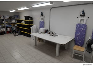 This is a photograph of an interior domestic space showing a utility room or storage area with organized shelving, household items, and appliances. The room appears to be part of a residential property, featuring storage solutions, ironing boards, an
