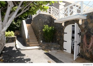 This photograph documents an exterior courtyard or entryway area of a property, featuring stone construction, landscaping, and architectural details including white lattice work and a storage structure. The image appears to be evidence documentation 