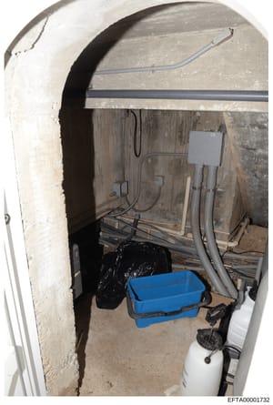This is an evidence photograph showing an underground or basement mechanical room with electrical and plumbing infrastructure. The space contains electrical conduit, wiring, a blue plastic basin or drip tray, PVC piping, what appears to be a water he