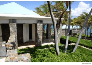 This is a photograph of a contemporary waterfront residence featuring stone and white architectural elements, palm trees, manicured landscaping, and ocean views. The image documents the exterior appearance of what appears to be a high-end coastal pro
