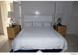 This is a photograph of a master bedroom interior featuring a large bed with white linens, matching wooden nightstands with lamps and decorative globes, and light gray-blue wall paneling. The image appears to be documentation of a residential propert