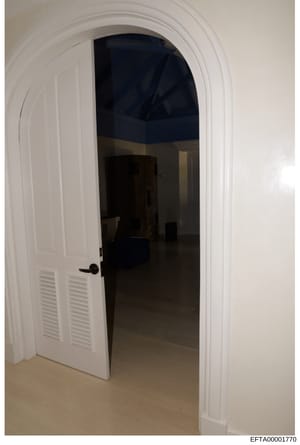 This is a photograph of an interior doorway featuring white trim with an arched molding and a white louvered door. The room beyond the doorway appears to have dark/navy blue walls or ceiling and minimal furnishings. The photograph was taken as part o