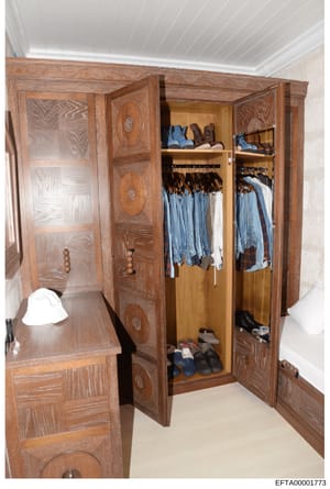 This is an evidence photograph showing the interior of a large wooden wardrobe or closet cabinet containing organized clothing, including blue jeans, white garments, and various shoes on shelves. The wardrobe features decorative wooden panels with in