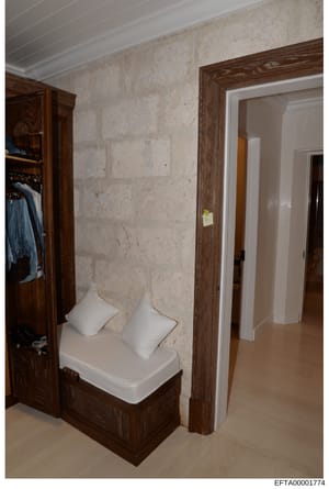 This is a photograph of an interior residential space, likely a dressing room or walk-in closet area. The image shows built-in wooden cabinetry with dark wood framing, cream/beige colored stone or marble walls, white bedding/cushions on a bench seat,