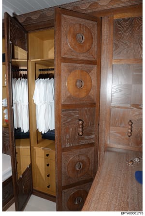 This photograph shows a custom-built wooden closet or dressing room with ornate oak cabinetry featuring circular decorative inlays. The closet contains multiple white garments hanging on black rods. The image documents residential interior furnishing