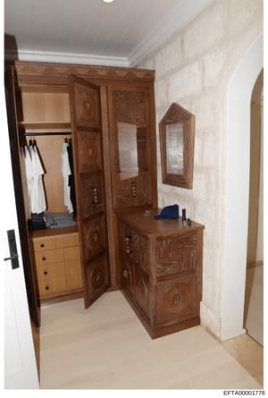 This photograph depicts a high-end residential closet and dressing room featuring custom wooden furniture, built-in storage, and mirrors. The space shows ornate wooden cabinetry with detailed carving, a vanity with mirror, clothing storage with hangi