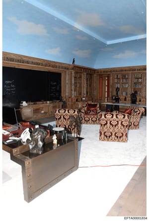 This is an evidence photograph showing the interior of an elaborately decorated room, likely from one of Epstein's properties. The space features custom wood-paneled walls with built-in bookshelves, ornate patterned furniture, a large black chalkboar