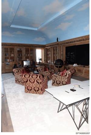 This photograph shows an elaborately decorated library or study room featuring custom wooden bookshelves, ornate upholstered furniture, and a distinctive ceiling with sky-blue muraling and recessed lighting. The room contains office equipment, a glob