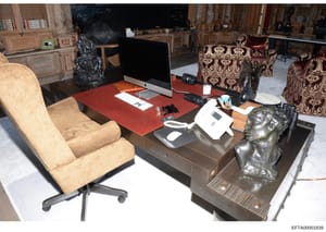 This is an evidence photograph showing a luxuriously appointed office interior with high-end furniture, artwork, and technology equipment. The space features ornate architectural details, expensive decorative objects including bronze sculptures, and 
