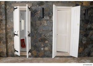 This photograph shows an interior hallway or corridor with two white painted double doors with black hardware, set against a distinctive mottled gray and brown stone or marble wall. A red fire extinguisher is visible inside the left doorway. The imag