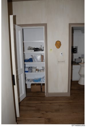This is an evidence photograph showing an interior hallway from what appears to be a residential property under investigation. The image documents a storage closet with white shelving containing various household items and supplies, a bathroom entran