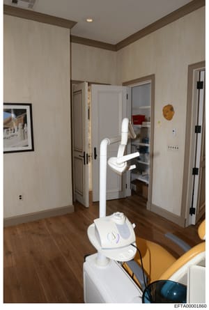 This photograph shows the interior of what appears to be a medical or dental treatment room, featuring professional equipment including a dental chair apparatus with articulated white arms, recessed lighting, modern finishes, and multiple doorways. T