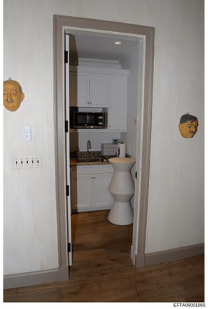 This is an evidence photograph showing the interior of a residential property, depicting a kitchen entrance with white cabinetry, appliances, and distinctive decorative mask sculptures mounted on the walls. The photo documents the property's interior