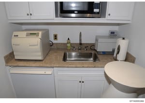 This photograph documents a compact kitchen or medical facility space, showing countertop appliances including an M9 UltraClave sterilizer, sink, microwave, and various medical/laboratory equipment. The image appears to be from a property seizure or 