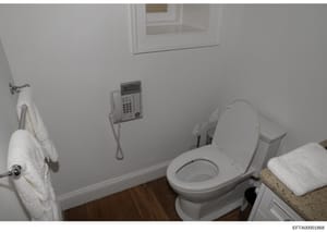 This is an evidence photograph of a bathroom interior showing a toilet with seat, sink with countertop, wall-mounted telephone, towel rack, and cabinet storage. The image appears to be from a property inspection or evidence documentation related to t