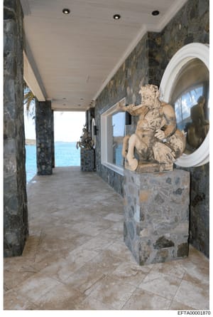 This photograph documents an interior hallway or corridor of what appears to be a luxury oceanfront property, featuring stone walls, a white ceiling with recessed lighting, and a classical stone sculpture of a cherub or putto on a pedestal. The hallw