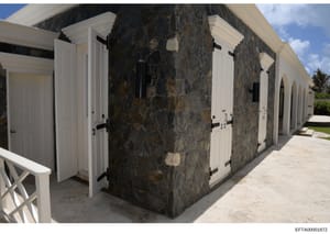This is a photograph of an outdoor structure featuring dark stone walls with white-trimmed doors and hardware. The building appears to be a poolhouse, cabana, or similar outbuilding at a residential property. The image shows the architectural details