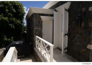This is a photograph of an exterior area of a property featuring a stone building with white trim, a covered walkway with white railings, and white wooden doors/entry points. The image appears to be documentation of property features, possibly relate