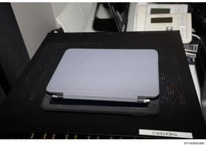 This is a photograph of a silver laptop computer (appears to be an HP or similar model) placed on a black textured mat, likely taken during an evidence collection or forensic examination. The laptop is positioned in what appears to be an office or in