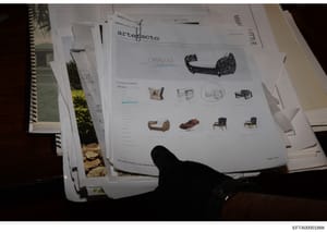 This photograph shows a collection of printed materials including an Artefacto furniture catalog and architectural/interior design documents. The catalog displays contemporary furniture pieces including upholstered seating, tables, and chairs. This a